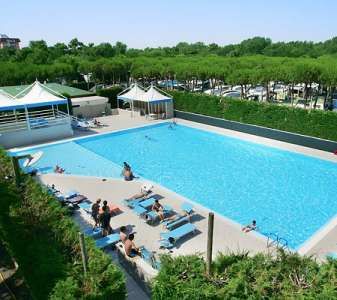 Piscina all'aperto con sdraio e persone che si rilassano, circondata da vegetazione.