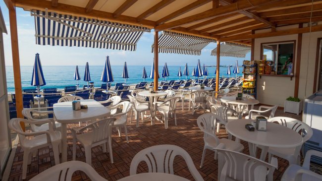 Terrazza sul mare con tavoli bianchi e vista sulla spiaggia.