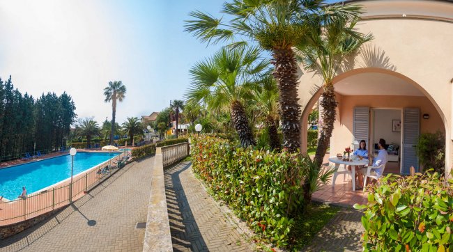 Terrazza con tavolo, attigua a piscina e palme.