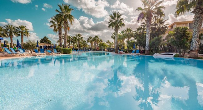 Piscina con palme e cielo nuvoloso.