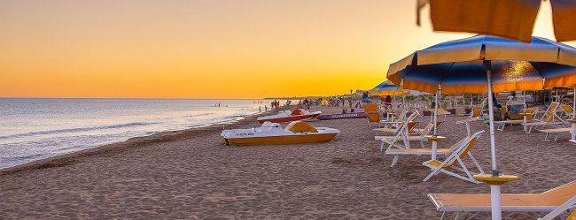 Spiaggia al tramonto con ombrelloni e pedalò.