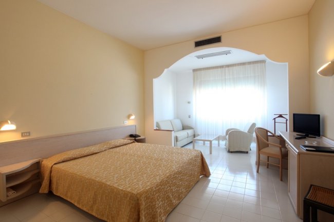 Camera da letto luminosa con letto matrimoniale e area salotto.