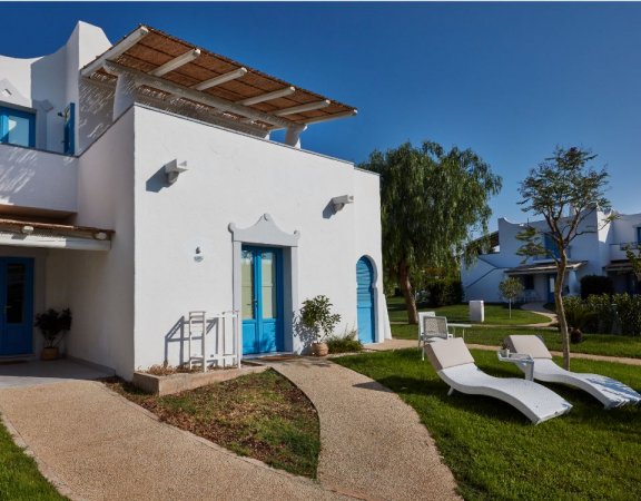 Casa bianca con dettagli blu e sedie a sdraio nel giardino.