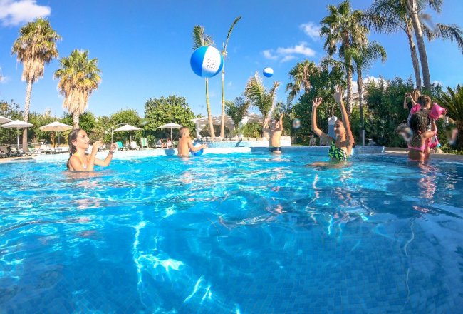 Persone che giocano in piscina sotto il sole estivo.