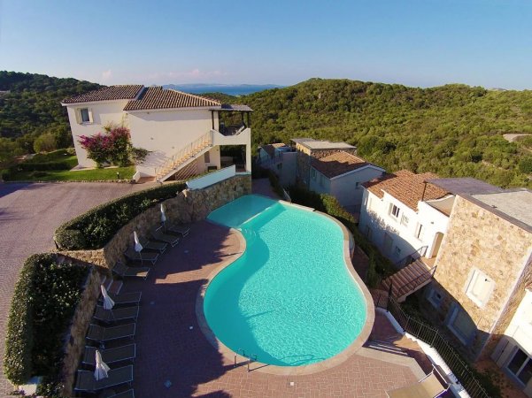 Piscina a forma di fagiolo circondata da edifici e colline.