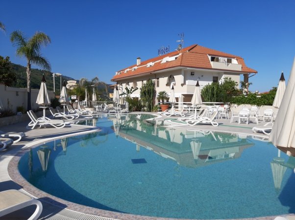 Piscina diurna con lettini e ombrelloni bianchi.