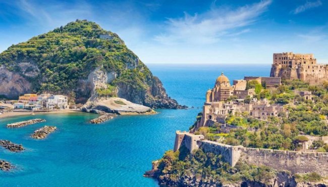Castello su un'isola con mare blu e vegetazione rigogliosa.