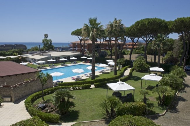 Giardino con piscina, ombrelloni e palme vicino al mare.