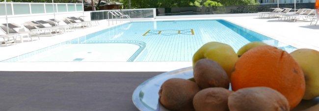 Piscina con sedie a sdraio, piatto di frutta in primo piano.