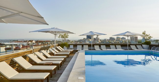 Piscina sul tetto con lettini e ombrelloni bianchi.