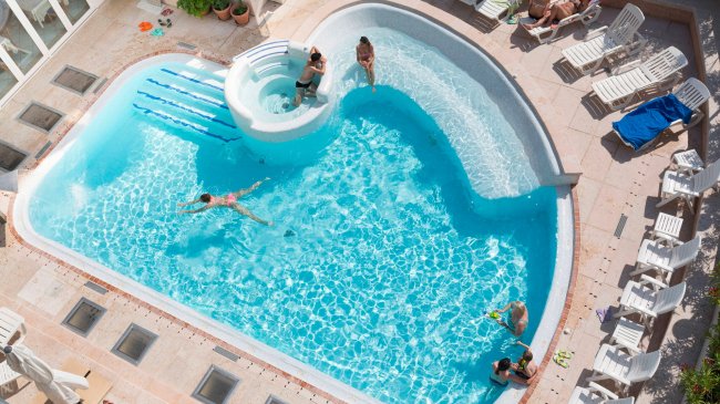Piscina esterna con persone che nuotano e prendono il sole.