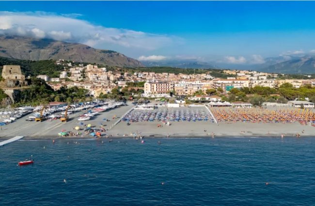 Spiaggia con lettini, mare e montagne sullo sfondo.