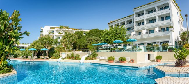 Piscina con ombrelloni verdi e hotel sfondo.