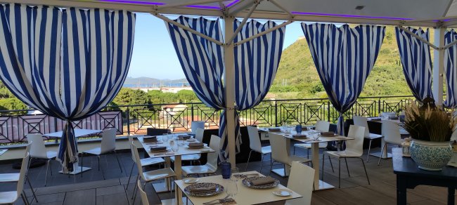 Terrazza con tavoli apparecchiati e tende a righe blu.