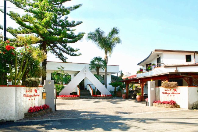 Ingresso di un hotel con palme e fiori.