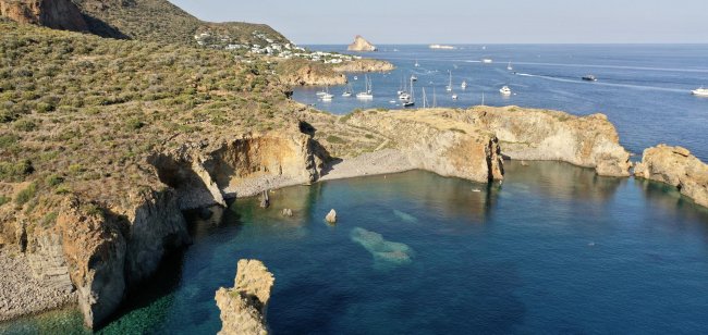 Baia con scogli e barche in lontananza.