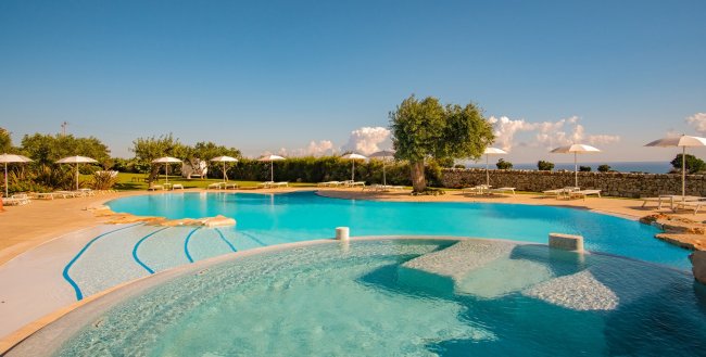 Ampia piscina con ombrelloni bianchi e cielo sereno.