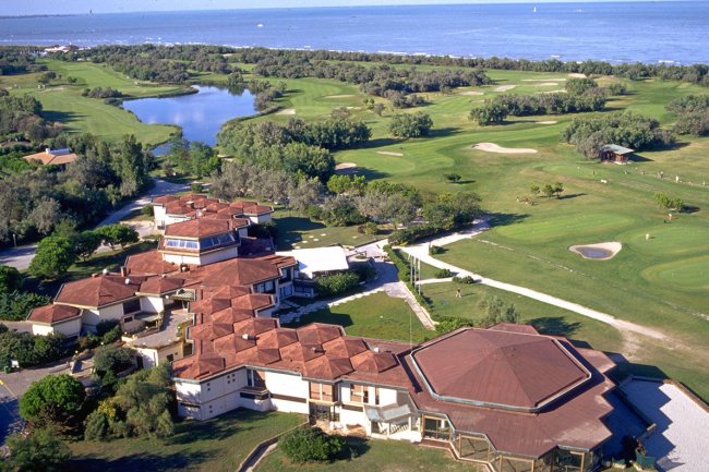 Vista aerea di un edificio con tetto rosso e campi da golf vicino al mare.