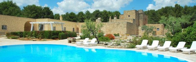 Piscina blu con lettini bianchi, edificio storico sullo sfondo.
