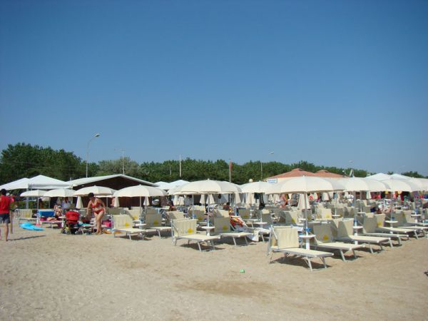 Spiaggia con lettini e ombrelloni beige, persone e cielo azzurro.