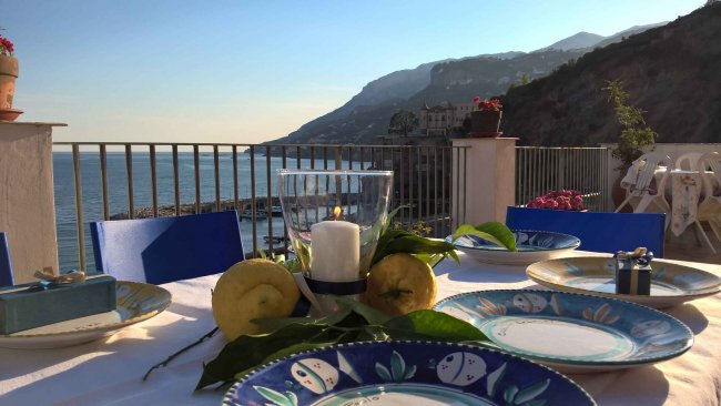 Tavola apparecchiata su terrazza vista mare e montagne.