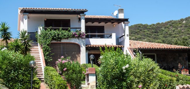 Casa bianca con balcone, scale esterne e piante rampicanti.