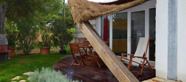 Terrazza con sedie e tavolo in legno, circondata dal verde.
