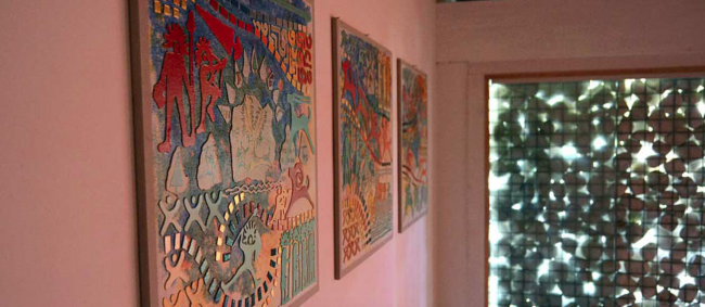 Quadri colorati su un muro rosa con luce filtrata.