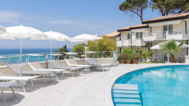 Piscina con lettini e ombrelloni bianchi, vista mare.