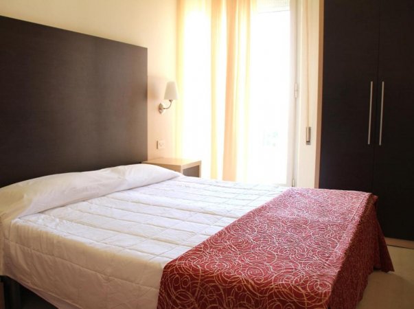 Camera da letto con letto matrimoniale e lenzuola bianche.