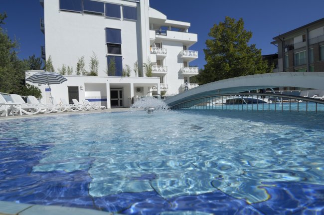 Piscina soleggiata con ponte e sedie a bordo.