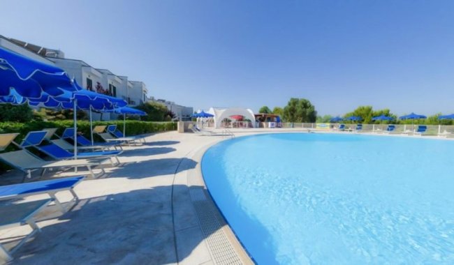 Piscina all'aperto con lettini e ombrelloni blu sotto un cielo sereno.