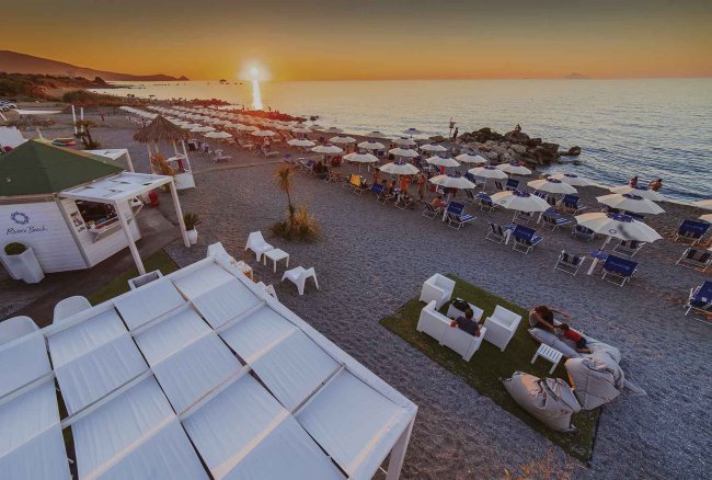 Spiaggia al tramonto con ombrelloni bianchi.