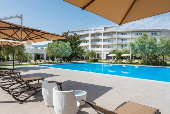 Piscina con lettini e ombrelloni, hotel sullo sfondo.