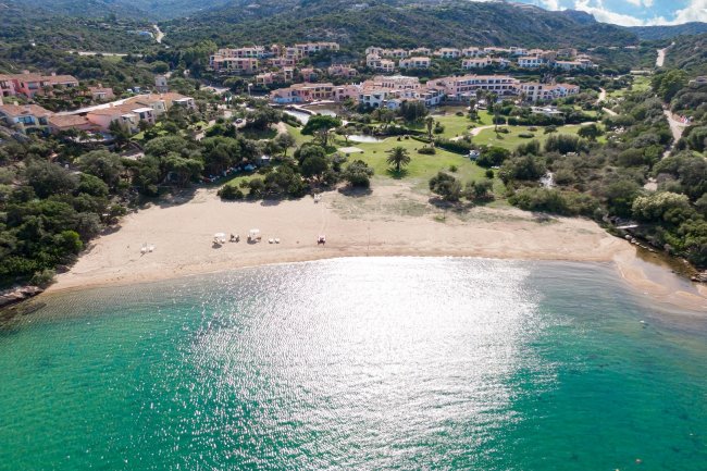 Spiaggia e mare turchese con complesso residenziale sullo sfondo.
