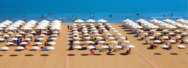 Spiaggia con ombrelloni bianchi e persone in mare.