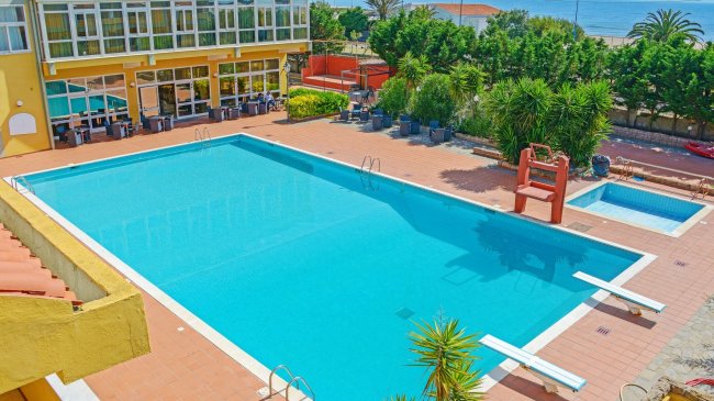 Grande piscina esterna con lettini e vegetazione attorno.