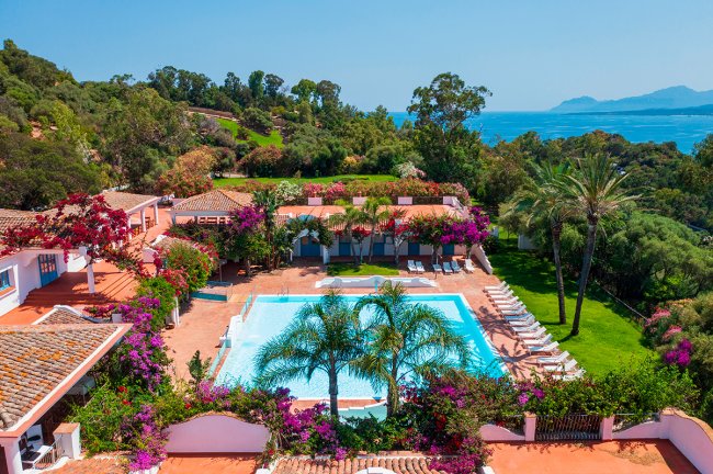 Piscina circondata da vegetazione e fiori colorati, vista mare.