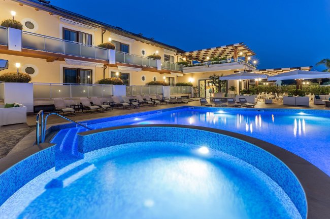 Hotel illuminato con piscina e sedie a sdraio.
