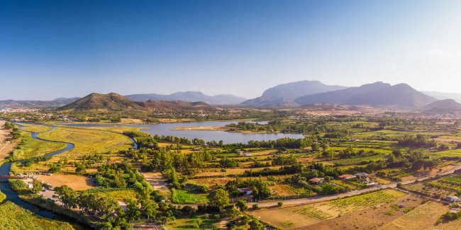 Panorama con lago, campi verdi e montagne distanti.