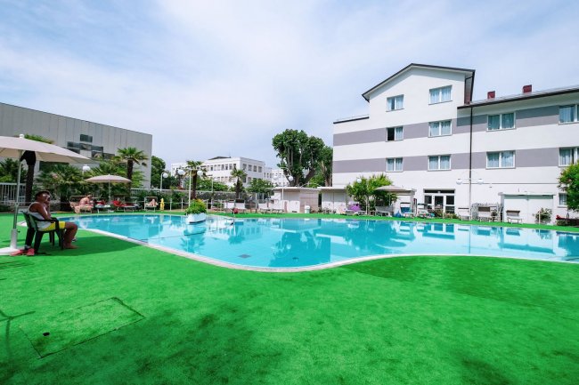 Piscina all'aperto circondata da edifici e ombrelloni.