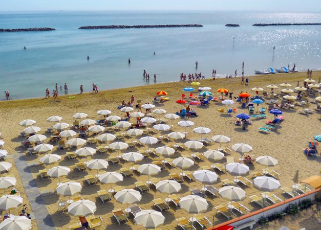 Spiaggia con ombrelloni bianchi e persone in mare.