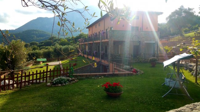 Casa rurale con giardino fiorito e montagna sullo sfondo.