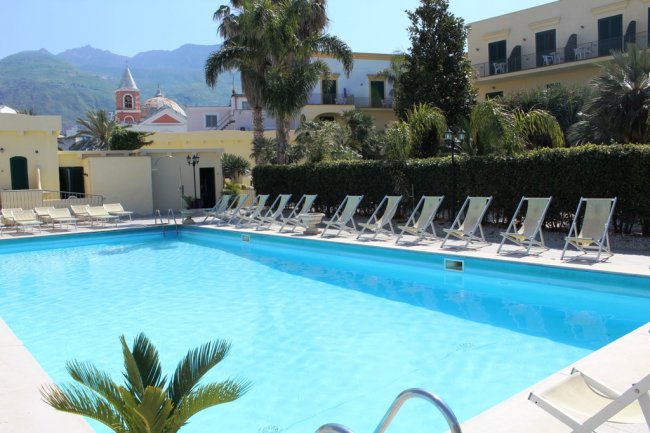 Piscina in un cortile con sdraio e palme, montagne sullo sfondo.
