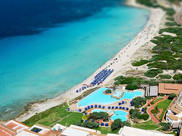 Spiaggia con lettini, acqua cristallina e piscina.