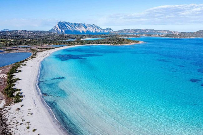 Spiaggia con mare azzurro e montagna sullo sfondo.