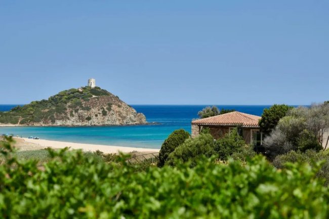 Vista mare con torre su un promontorio e vegetazione rigogliosa.