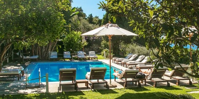 Piscina circondata da lettini e ombrelloni; giardino verde.