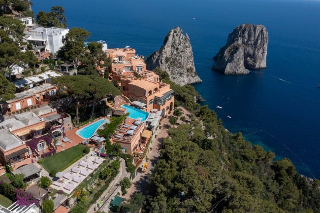 Panorama aereo di un hotel con piscina e faraglioni.