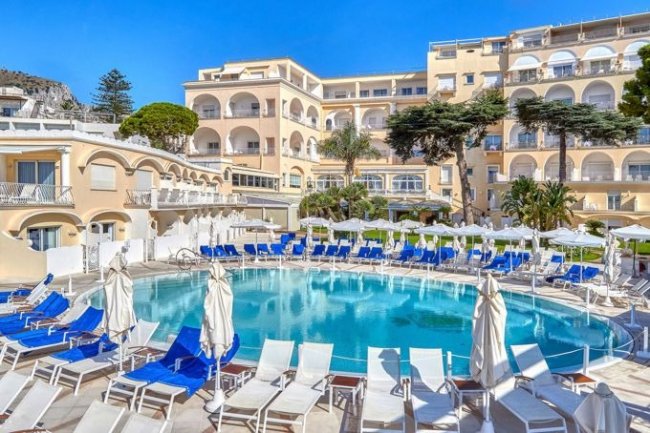 Una piscina circondata da lettini bianchi e azzurri, con un edificio in sfondo.